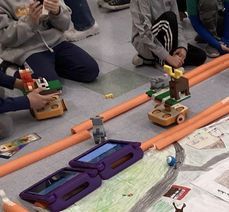 Orange pool noodles create a path for KIBO robots carrying various animals. 